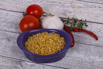 Raw bulgur in the bowl with tomatoes and garlic