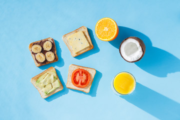 Sandwiches, glass with orange juice, coconut, oranges, blue background. The concept of healthy eating, breakfast at the hotel, diet. Natural lighting, hard light. Flat lay, top view.