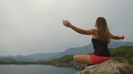 Fototapeta na wymiar Female tourist sitting on a rock on clear sky and calm sea background