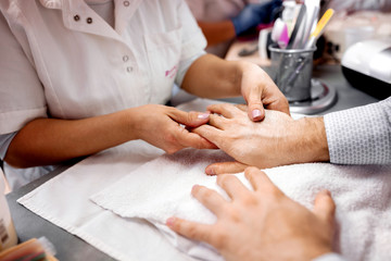 Fototapeta na wymiar Manicurist making physical contact with her client by holding his hand during manicure grooming treatment