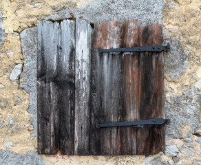 Sehr alter, geschlossener Fensterladen aus verwittertem Holz in einer ruinösen Fassade
