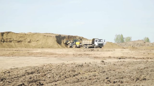 Bulldozer loading sand transportation truck on construction site. Construction equipment. Crawler bulldozer moving sand.
