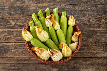 Many very fresh zucchinis with their flowers in a bowl on the rustic table