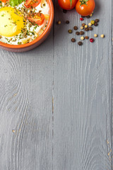 Portioned baked eggs in ceramic cocotte on gray wooden table, breakfast. Top view, copy space for you text.