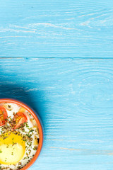 Portioned baked eggs in ceramic cocotte on blue wooden table, breakfast. Top view, copy space for you text.