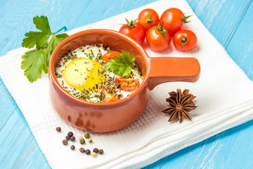 Portioned baked eggs in ceramic cocotte on blue wooden table, breakfast.