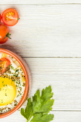 Portioned baked eggs in ceramic cocotte on white wooden table, breakfast. Top view, copy space for you text.