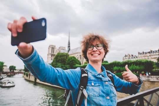 Caucasian female tourist photographing themselves by mobile telfon on background Notre Dame Cathedral from bridge over Seine bridge arsheveshe. Image Cathedral of Notre Dame de Paris