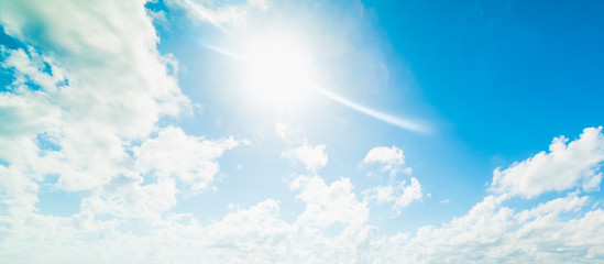 Sun shining over a blue sky with white, soft clouds