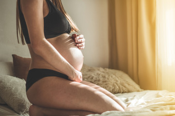 Attractive pregnant woman is sitting in bed and holding her belly. Last months of pregnancy