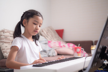 Asian little girl learning to play piano keyboard synthesizer with happiness