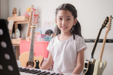 Asian little girl learning to play piano keyboard synthesizer and smile with happiness