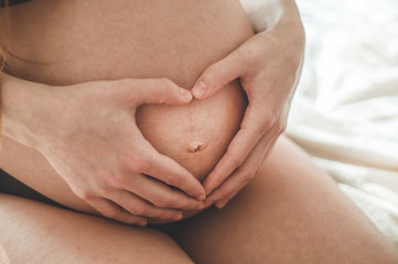 Attractive pregnant woman is sitting in bed and holding her belly. Last months of pregnancy