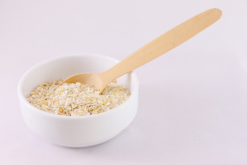 Oatmeal with yellow apricot pieces in a deep white bowl, a wooden spoon, a jar of milk.