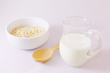 Oatmeal with yellow apricot pieces in a deep white bowl, a wooden spoon, a jar of milk.