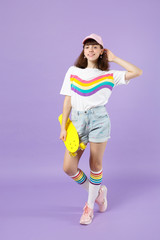 Portrait of pretty teen girl in vivid clothes holding yellow skateboard, putting hand on head isolated on violet pastel wall background. People sincere emotions, lifestyle concept. Mock up copy space.