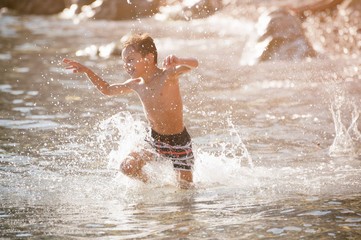 happy delightful little caucasian boy running through sea water with splashes in sunny warm summer leisure day