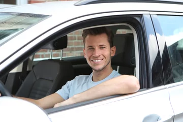 Fotobehang Junger Mann sitzt lachend in einem Auto © Joerch