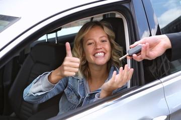 Junge Frau sitzt in einem Auto und bekommt einen Schlüssel überreicht