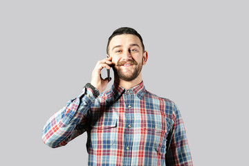 Young handsome man with facial hair posing over gray wall with a lot of copy space for text. Portrait of confident bearded male, wearing hipster slim fit checkered shirt. Isolated, background.