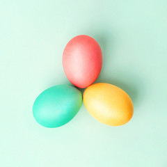 Three colorful Easter eggs in triangle on mint colored background. Flat lay.