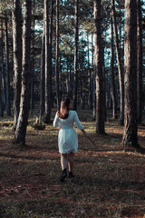 oung woman walking away alone on a forest path wearing a white dress