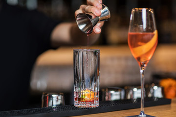 Bartender is adding ingredient in shaker at bar counter.