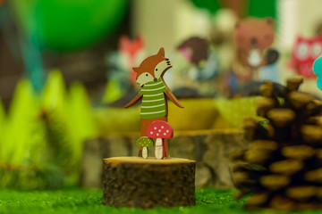 A coarse plan of a toy ladder in a green striped T-shirt with mushrooms, next to a large pine cone herringhouse tree