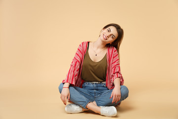 Portrait of smiling beautiful young woman in casual clothes sitting, looking camera isolated on pastel beige wall background in studio. People sincere emotions, lifestyle concept. Mock up copy space.