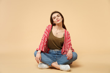 Portrait of tender pretty young woman in casual clothes sitting, looking camera isolated on pastel beige wall background in studio. People sincere emotions, lifestyle concept. Mock up copy space.