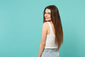 Fototapeta premium Back rear view of attractive cute young woman in light casual clothes looking back isolated on blue turquoise wall background in studio. People sincere emotions, lifestyle concept. Mock up copy space.