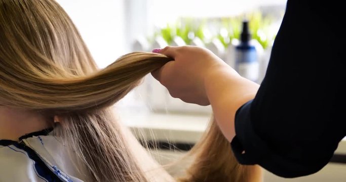 The hairdresser dries and combs a long fair hair. Hairdressing salon. 4K UHD