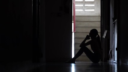 Silhouette of a sad young girl sitting in the dark leaning against the wall in old condo, Domestic violence, family problems, Stress, violence, The concept of depression and suicide.