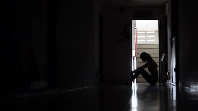 Silhouette of a sad young girl sitting in the dark leaning against the wall in old condo, Domestic violence, family problems, Stress, violence, The concept of depression and suicide.