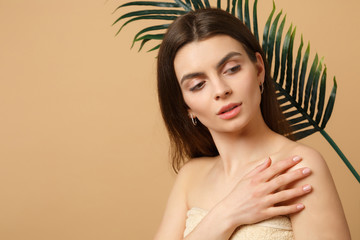 Close up brunette half naked woman 20s with perfect skin, nude make up palm leaf isolated on beige pastel wall background, studio portrait. Health care cosmetic procedures concept. Mock up copy space.