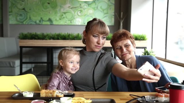 Grandmother's daughter and granddaughter are photographed on the phone in a cafe A young woman takes a picture of herself on a smartphone with an elderly mother and little daughter