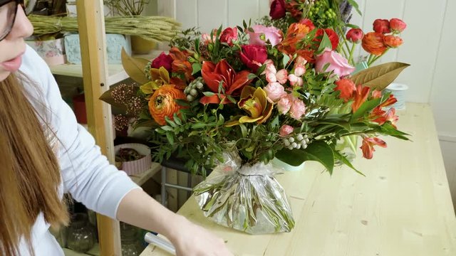 Female florist in flower shop. Woman making a beautiful and stylish bouquet of fresh flowers in floral design studio. 4K