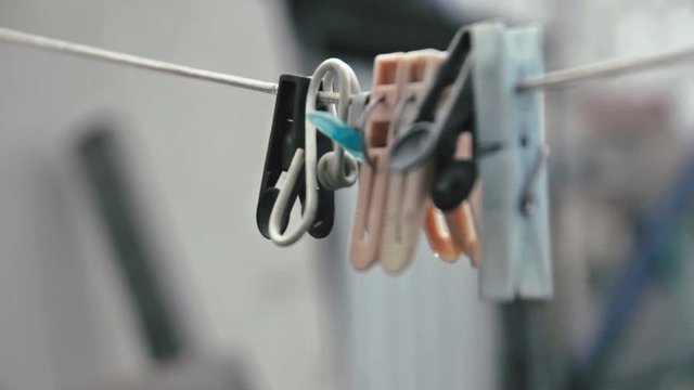 Clothespins hang on a rope swinging in the wind on backyard on cloudy day.