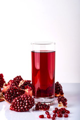 Glass of juice with a some pieces of pomegranate on a white background.