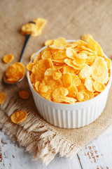 Bowl with golden flakes on a linen, on a light wooden table, next to a spoon. Rustic country style. View from above