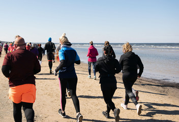 A group of back lit people in colorful outfits are running during a marathon that goes partly over a beach in Jurmala, Latvia 14 April 2019