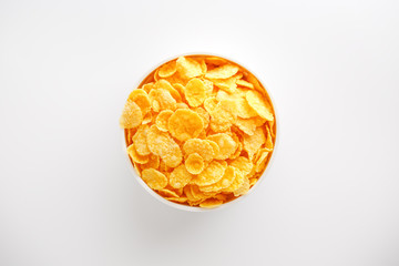White cup with golden corn flakes isolated on white background. View from above. Delicious and healthy breakfast