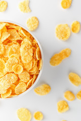 White cup with golden corn flakes, isolated on white background. Hopya crumbled around the cup. View from above. Delicious and healthy breakfast