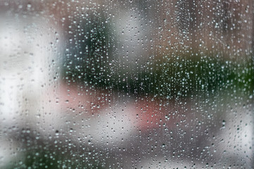 Glass window with raindrops. Overcast day and blurred cityscape outside. Symbol of sadness, depression, sorrow. Abstract texture background with copy space for text and design. Realistic image.