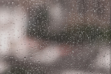 Glass window with raindrops. Overcast day and blurred cityscape outside. Symbol of sadness, depression, sorrow. Abstract texture background with copy space for text and design. Realistic image.