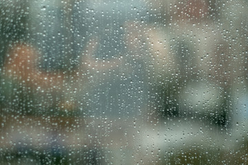Glass window with raindrops. Overcast day and blurred cityscape outside. Symbol of sadness, depression, sorrow. Abstract texture background with copy space for text and design. Realistic image.