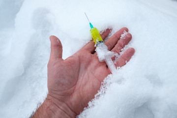 the open palm of the man who fell on the snow fell from the palm of a syringe with a liquid yellow