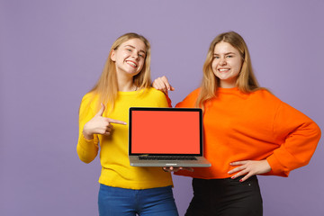 Two young blonde twins sisters girls pointing index finger on laptop pc computer with blank empty screen isolated on pastel violet blue background. People family lifestyle concept. Mock up copy space.