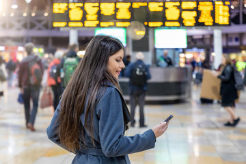 Young traveler woman looks at her mobile phone on a busy train station
