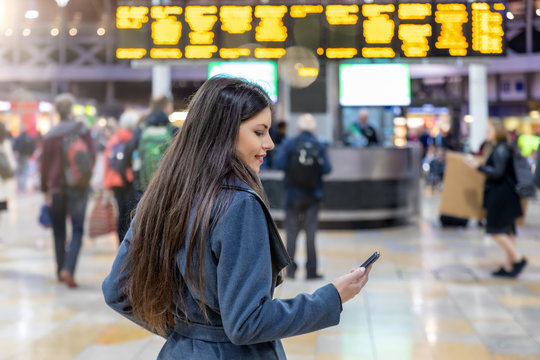 Young Traveler Woman Looks At Her Mobile Phone On A Busy Train Station